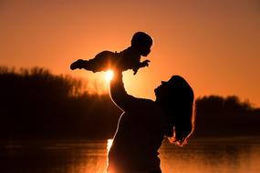 Silhouette of a mother with the baby on the beautiful coast with trees, at colorful sunset