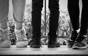 black and white photo of three pairs of legs of teenagers