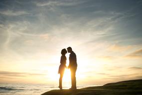 Silhouette of the couple, kissing on the beautiful beach, at colorful and beautiful sunset in the sky, with the clouds