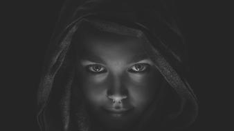 Black and white portrait of a woman, with the nose piercing, covered in the hood, among the darkness