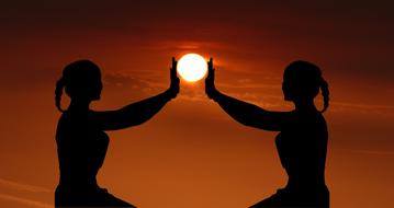 two silhouettes of girls hold the sun