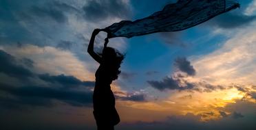 silhouette of a girl with a scarf against a cloudy sky