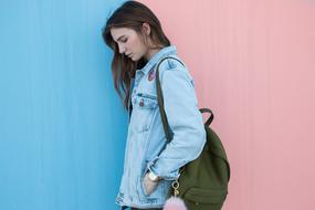 Profile portrait of a girl with green backpack, and in denim jacket, at the blue and pink background