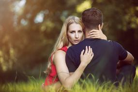 Couple, hugging, while sitting on the green grass, among the colorful trees, in light