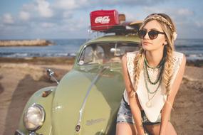 Beautiful blonde girl with the retro Beetle car on the beach