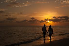 Silhouette of a couple, walking on the beautiful sandy beach, at colorful and beautiful sunset in the sky with clouds