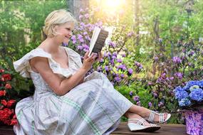 Smiling, blonde woman, reading a book, among the colorful and beautiful plants, in the garden