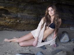 girl in a swimsuit on gray sand on a background of rock