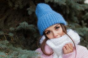 Portrait of the woman in blue hat and covered in white scarf, near the green fir tree