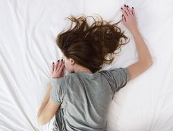 woman in grey dress lays on White Sheet