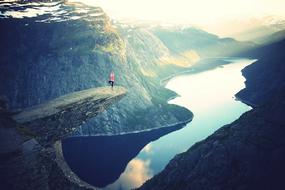 distant view of a man on a sheer cliff above a lake