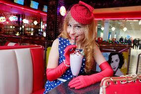 Pin-up girl in colorful clothing from 50s, drinking milkshake in the American cafe