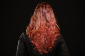 Back view of the woman with beautiful, pink and orange hair, at black background