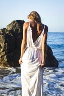 girl in a long white dress on a background of a boulder by the sea