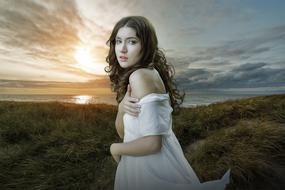 fantastic photo of a girl in a white dress on the green dunes by the sea against the background of sunset