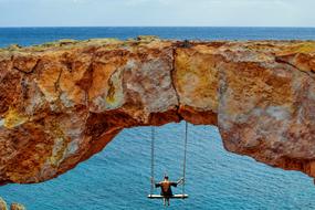 Back view of a person, hanging on the swing, on the beautiful and colorful cliff, on the shore