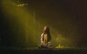 photo of a girl under the rays of the sun in a dark forest