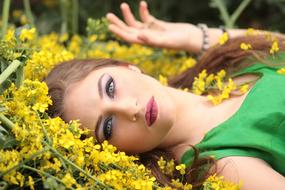 Portrait of the girl, with the make-up and in green dress, laying on the beautiful, yellow flowers