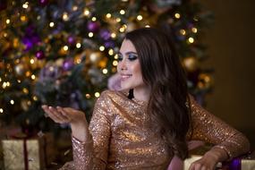 pretty Girl in golden dress sits in front of Christmas Tree