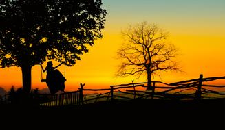 silhouette of a girl on a swing on a background of yellow sunset