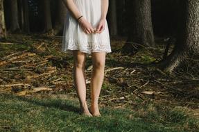 Standing woman, in the beautiful, patterned, white sundress, among the colorful plants in the forest