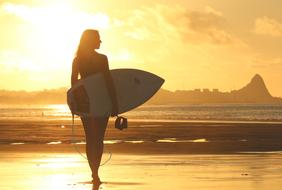Surfer girl on a beach at the sunset