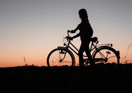 silhouette of a girl with a bicycle at sunset