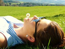 Portrait of the laying young woman with sunglasses on the beautiful and colorful meadow in spring