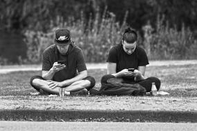 Black and white photo of the sitting couple, using smartphones, near the plants