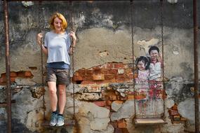 girl stands on a swing against the background of a ruined wall
