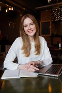 Portrait of a smiling woman in white clothing, with the notebooks on the table