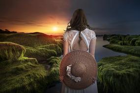 Woman with the hat on the landscape with the sunset