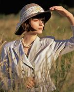 Beautiful woman in grey jacket and colorful hat, posing among the yellow and green grass