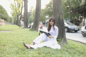 Portrait of Young asian Girl sitting with laptop beneath tree at road