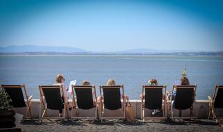 People, on the deck chairs, on the beach of the sea, in light, at background with the mountains