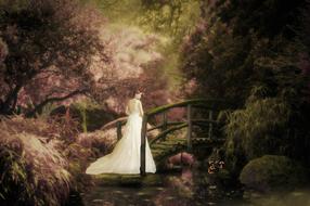 painted bride walks over a wooden bridge in a dense garden