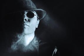 Portrait of a gangster with sunglasses and hat, among the smoke