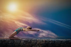 young man doing Yoga exercise on stone wall at sunset sky