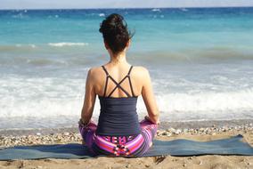Back view of the woman, meditating, on the sandy beach, near the colorful and beautiful sea