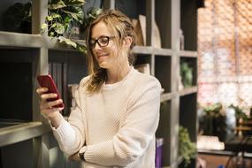 girl in glasses with a smartphone stands at the shelf