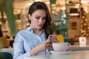 Portrait of the woman, with make-up, using smartphone and deinking coffee, at the restaurant