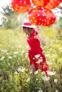 Young woman with the colorful balloons on the field of the colorul flowers