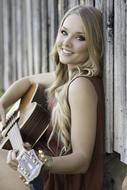 blonde with a guitar against a wooden wall