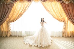 Bride in luxury dress at window with curtains