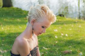 Profile portrait of a girl with blonde hairstyle, in black and white dress, on the green field with trees and colorful leaves