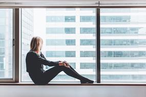 young girl sits on Window sill looking at opposit building
