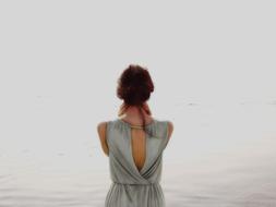 a woman in a gray dress stands on the background of the lake
