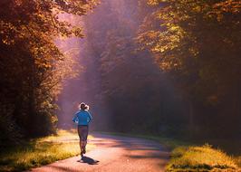 Woman, running on the beautiful road in sunlight, among the colorful plants, in the morning