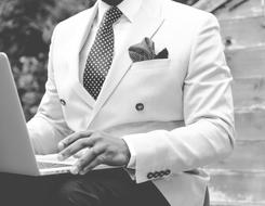 Black and white photo of the man, in the suit, using laptop on the knees