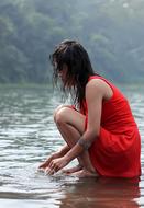girl in a red dress squatting on the lake